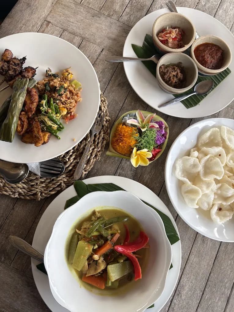 A Petulu class table with sate, banana-leaf pepes, sambal bowls, canang sari, krupuk, and coconut curry, on a food day near Ubud