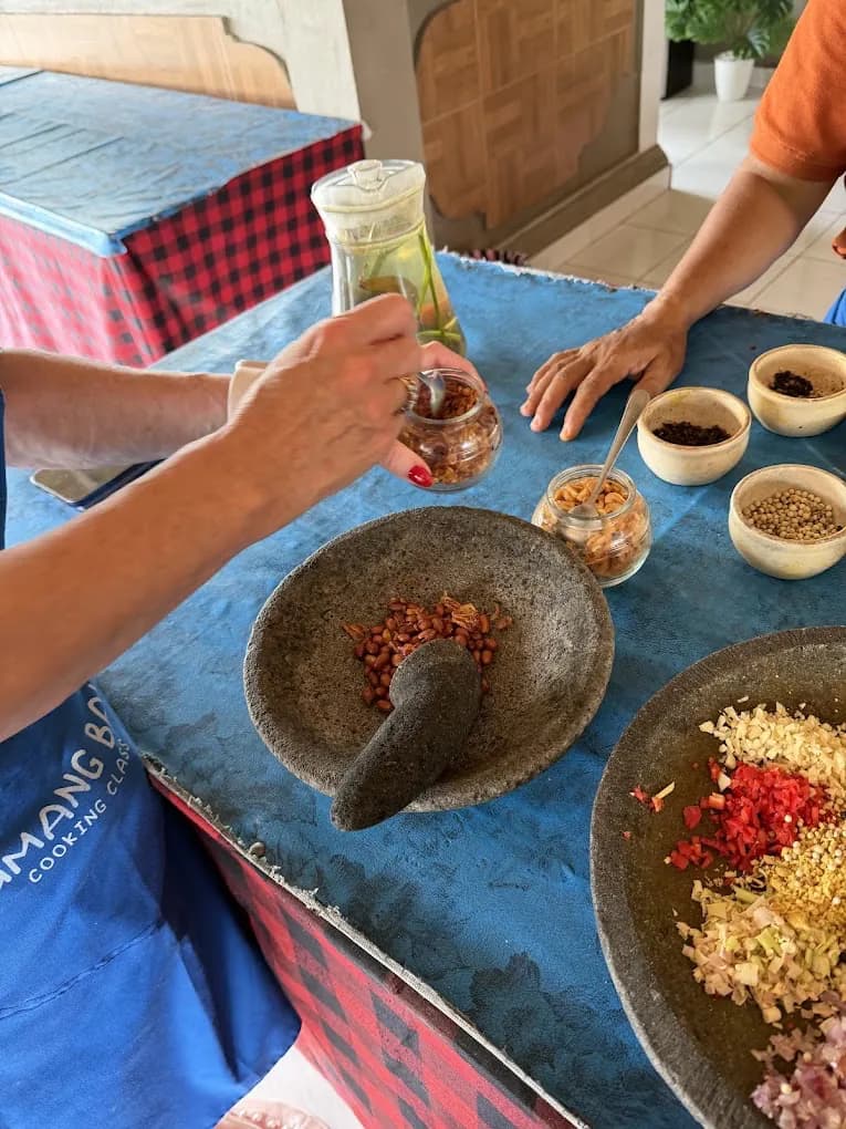 Hands grinding base genep in a stone mortar at the Petulu spice table, on a food day near Ubud