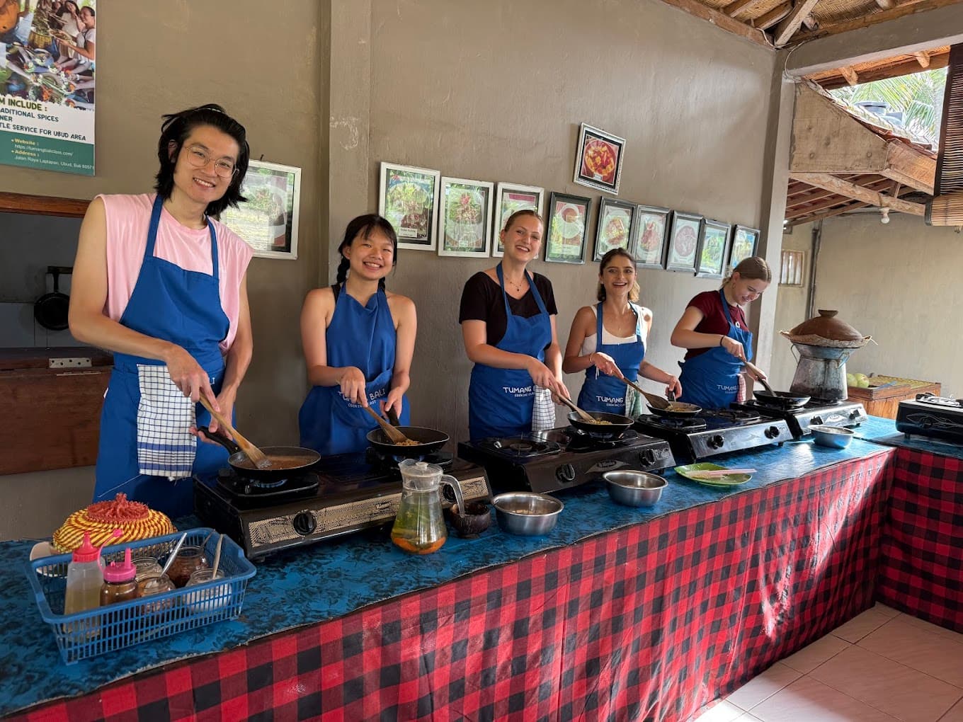A small group in blue aprons seated along a class table with bowls of ingredients, on a food day near Ubud