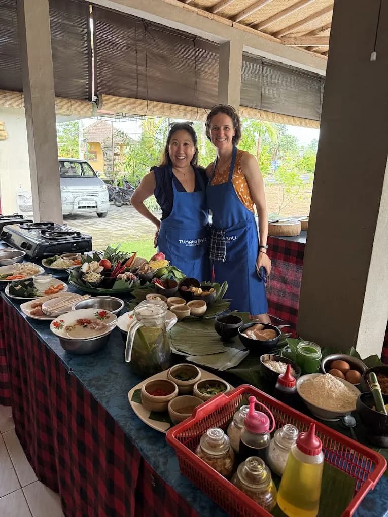 Two guests in Tumang Bali aprons cooking at the prep table in Petulu, on a food day near Ubud