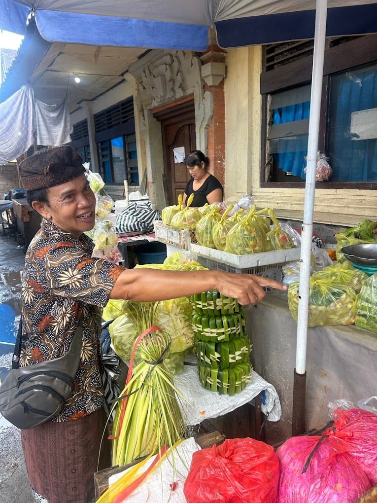 A morning market stall piled with chilies, shallots, and garlic, with a guide in a blue apron, on a food day near Ubud